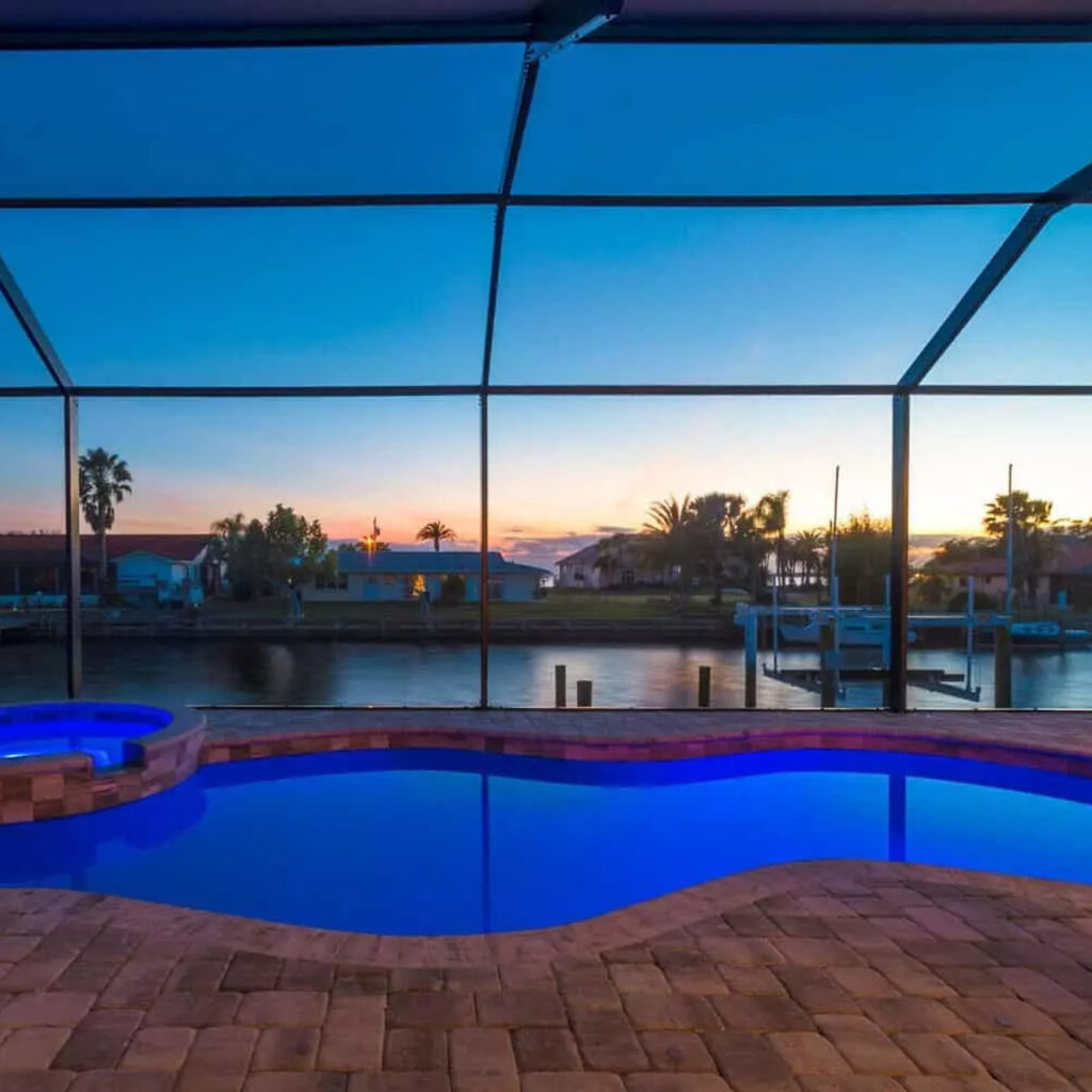 A screened lanai pool with freeform shape and raised spa overlooking a canal at dusk.