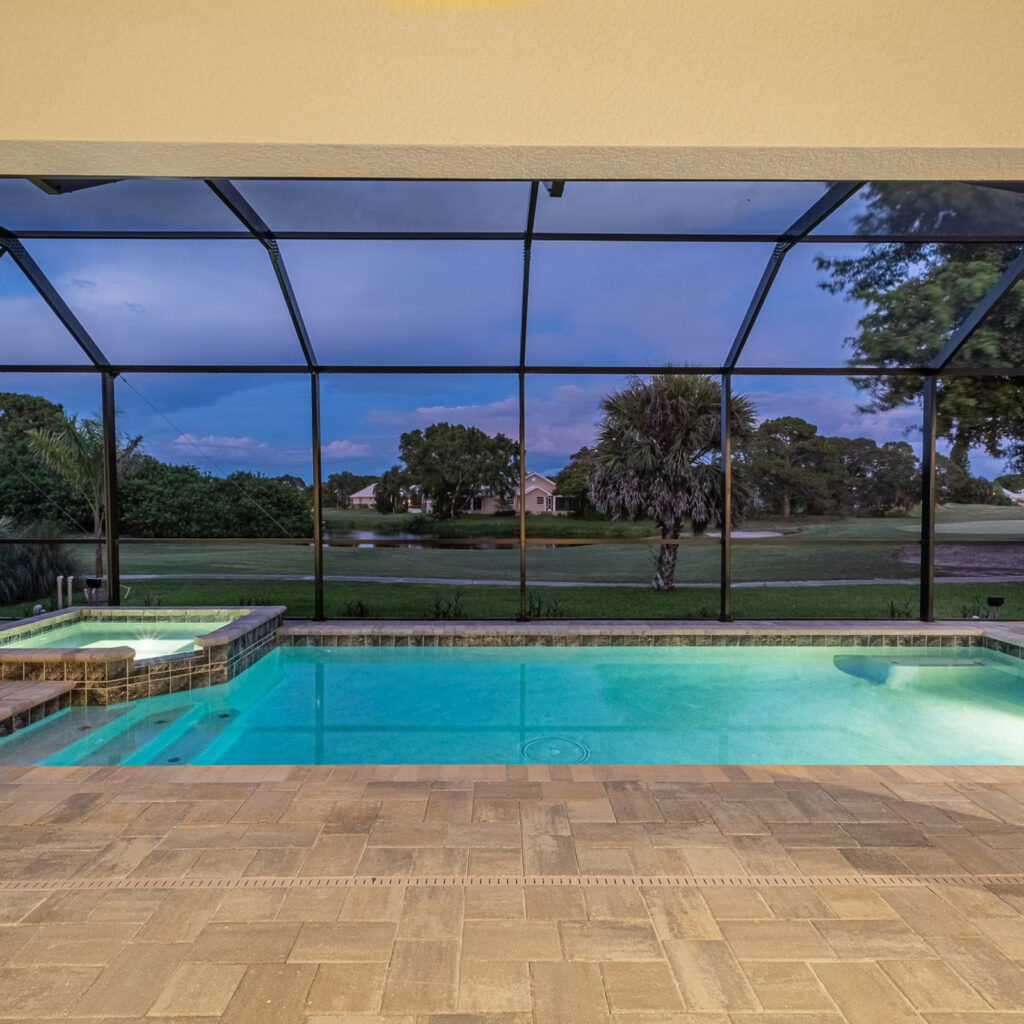 A screened rectangular pool with a raised spa overlooks a golf course at dusk.