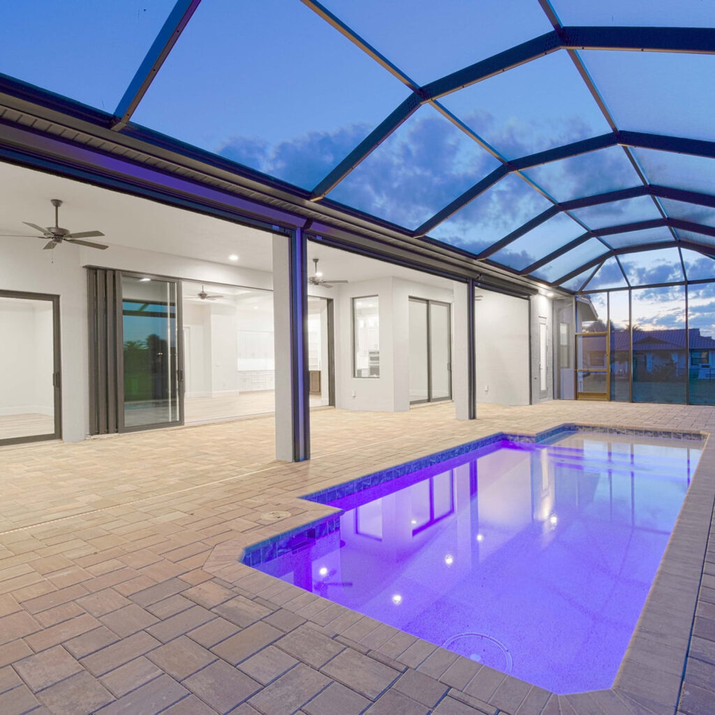 A rectangular pool lit purple by LED lights under a screened lanai at dusk.