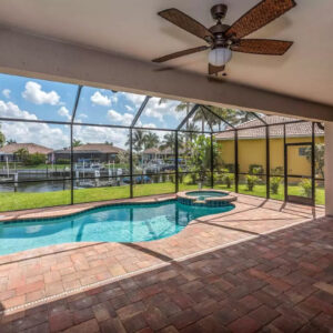 A screened lanai with a freeform pool and raised spa overlooking a canal lined with palm trees.