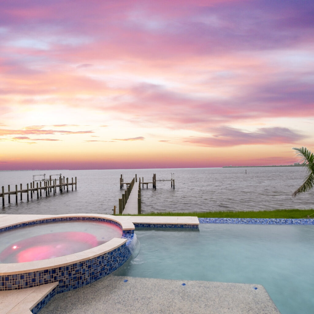 A raised mosaic-tiled spa spills into an infinity pool overlooking the bay at sunset.