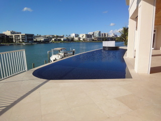 An infinity-edge pool on a waterfront terrace overlooking a marina and city skyline.