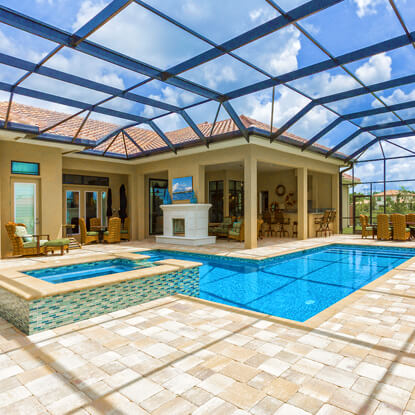 An L-shaped pool with a raised spa and tiled walls sits under a large screened enclosure beside an outdoor fireplace and kitchen.