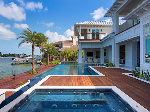 A raised spa with jets sits on a wood deck in front of a long lap pool overlooking the waterway.