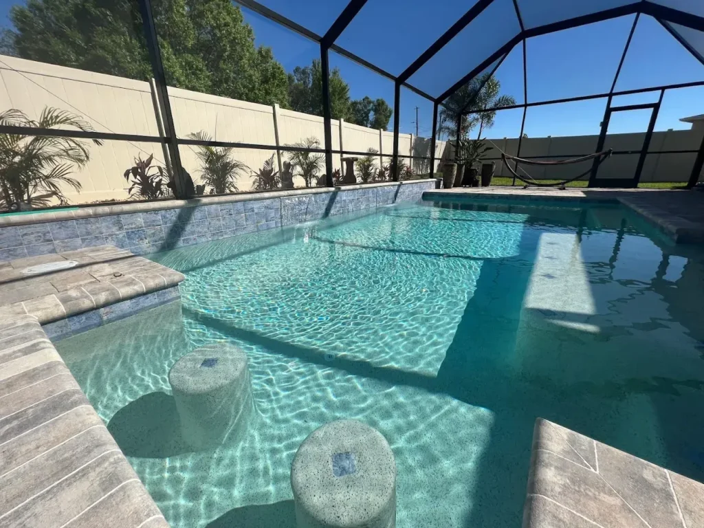 A screened backyard pool with a shallow tanning ledge and two submerged stone stools near the steps.