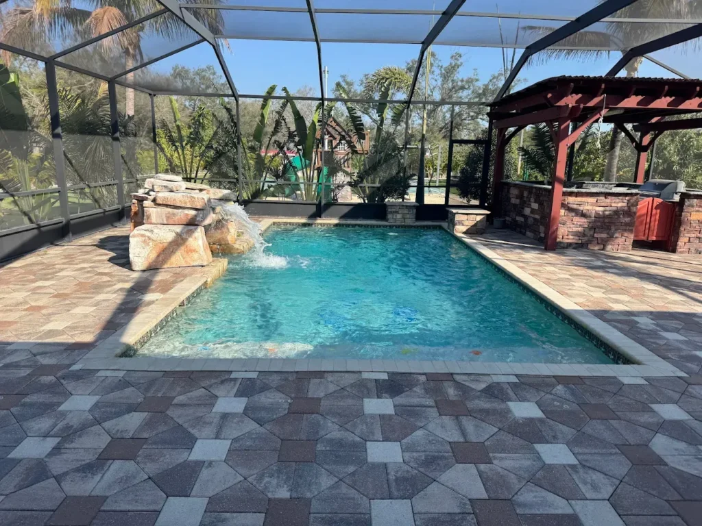 A screened rectangular backyard pool with a rock waterfall feature and paver decking.
