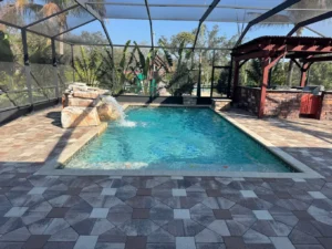 A screened rectangular backyard pool with a rock waterfall feature and paver decking.
