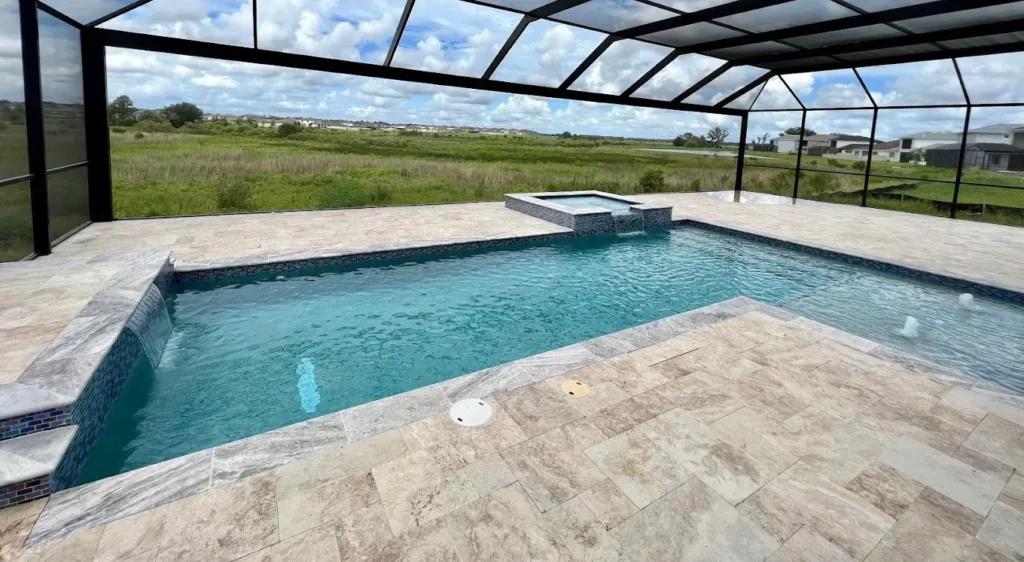 An L-shaped pool with a raised spa under a screened enclosure overlooking an open field.
