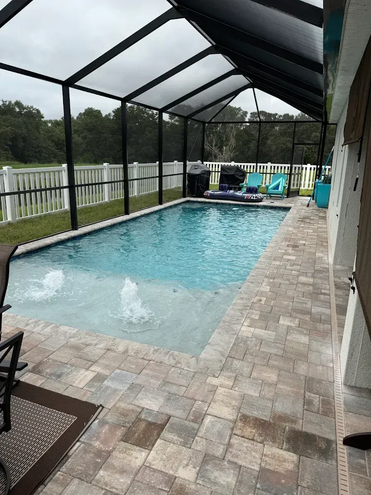 A small rectangular pool with bubbler jets under a screened enclosure with paver decking.