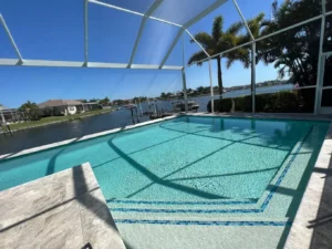 A screened, multilevel geometric pool with mosaic tile steps overlooking a canal with boats docked nearby.