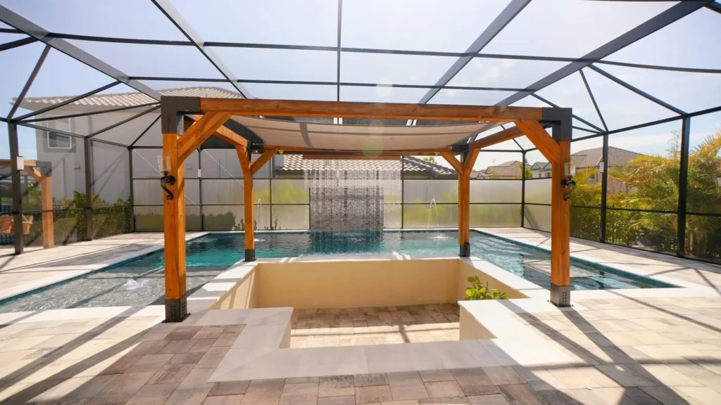 Rectangular pool under a screened lanai with a wooden pergola shade structure and a sheer descent water curtain feature over a sunken seating area.