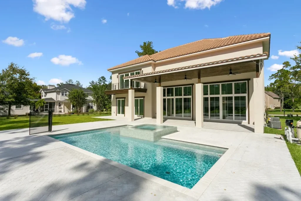 A rectangular pool with an attached raised spa on a stamped concrete patio behind a modern two-story home.