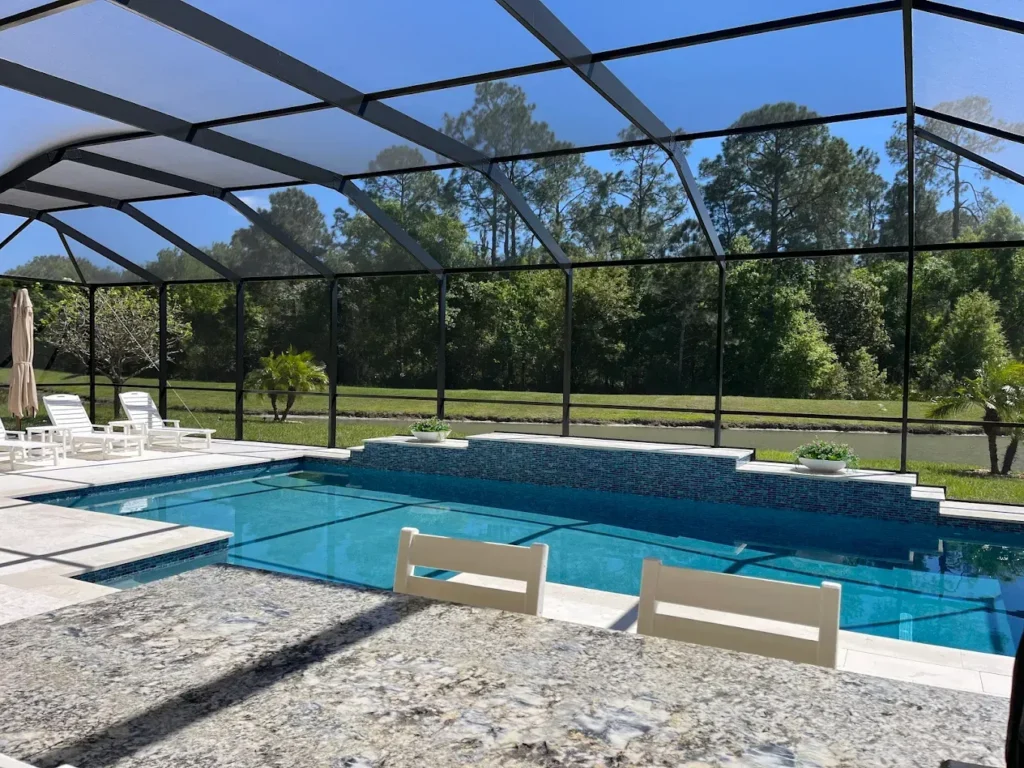 A screened rectangular pool with a raised tiled wall overlooking a canal and trees.