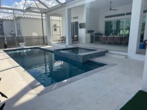 A rectangular pool with an attached raised spa and mosaic-tiled wall under a screened patio.