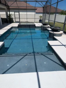 Rectangular pool with raised spa and two fire bowls under a screened enclosure.