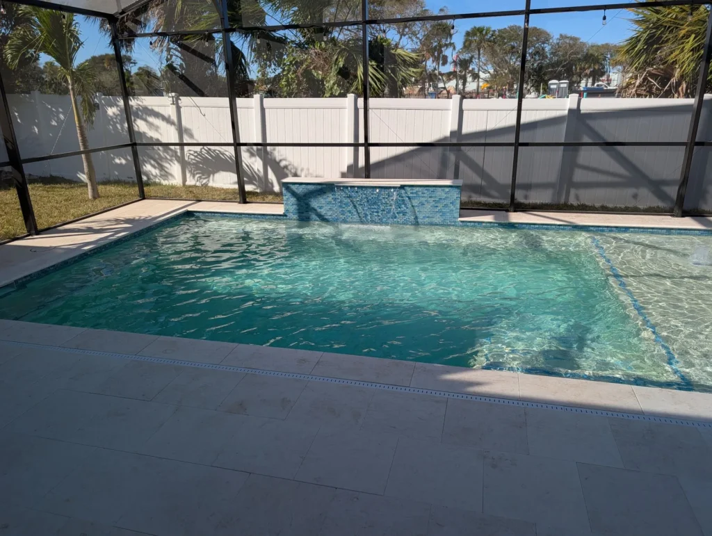A screened rectangular backyard pool with a raised tiled water-feature wall and travertine deck.
