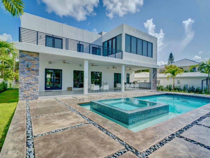 Modern two-story home with a rectangular pool and raised tiled spa on a paver patio under open sky.