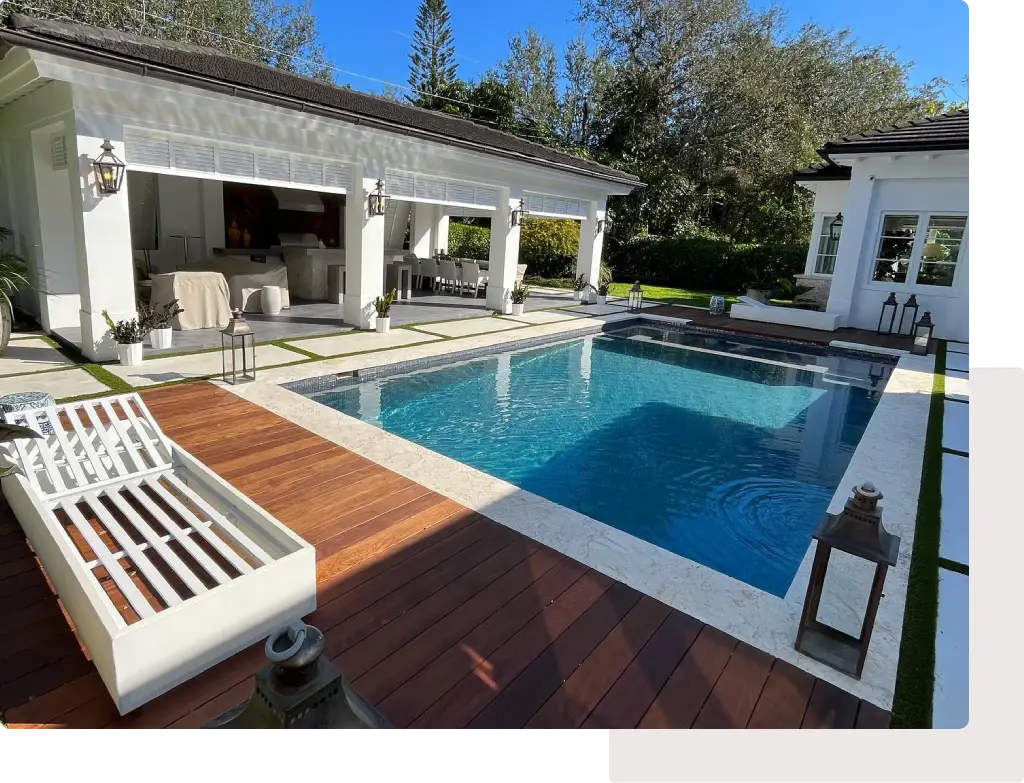 A rectangular backyard pool with a wood deck and pool house cabana in the background.