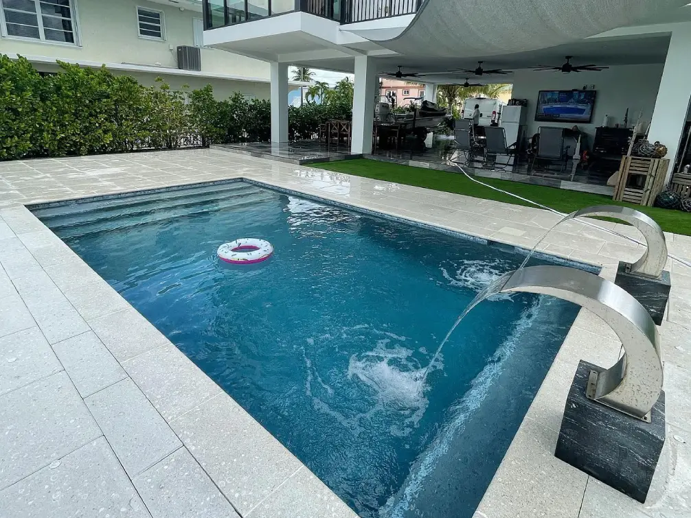 A small rectangular backyard pool with two stainless steel scupper water features and a floating pool ring, next to a covered patio.