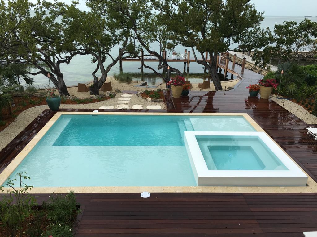 A rectangular infinity-edge style pool with a raised square spa on a wood deck overlooking the water.