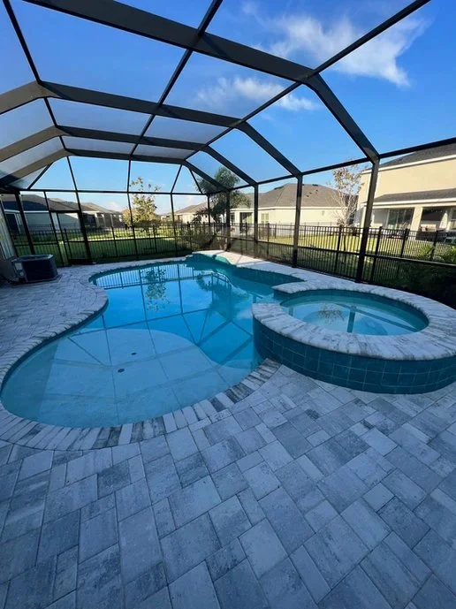 Freeform pool with raised round spa under a screened lanai enclosure and paver deck.