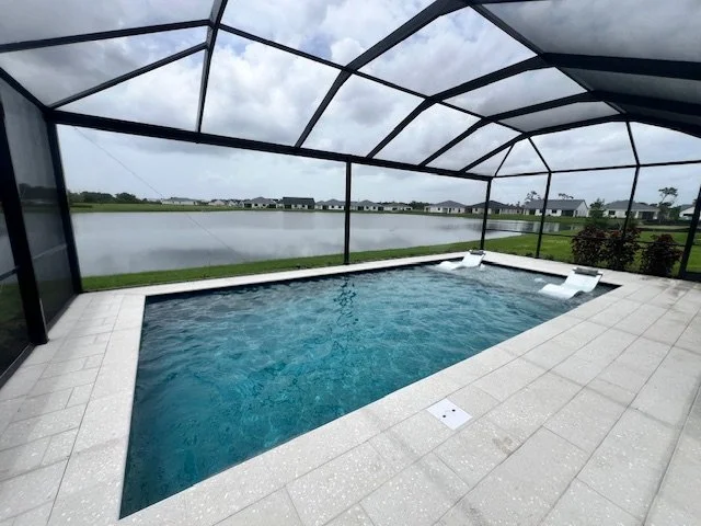 A screened rectangular pool with two in-water loungers overlooking a community lake.
