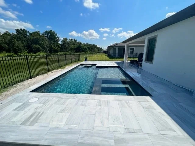 Rectangular pool with a raised spa and tanning ledge next to a modern house.