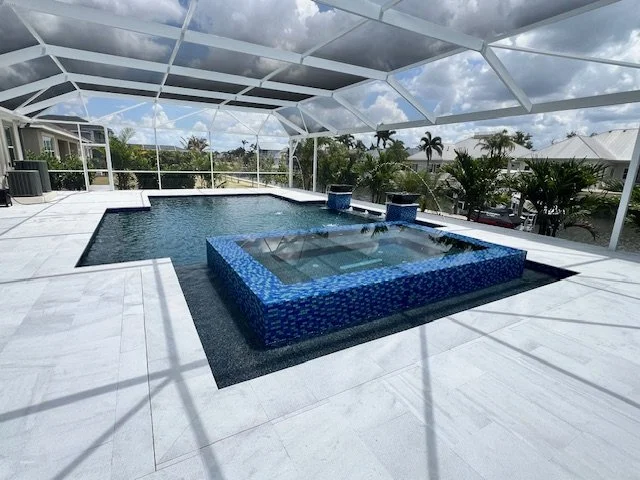 A rectangular pool with a raised tiled spa featuring spillover and fire bowls under a screened enclosure.