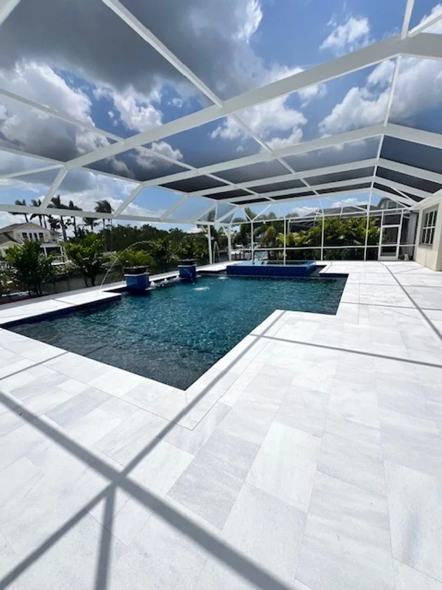 A screened lanai with an L-shaped pool, raised spa, and water bowl fountains overlooking a canal.