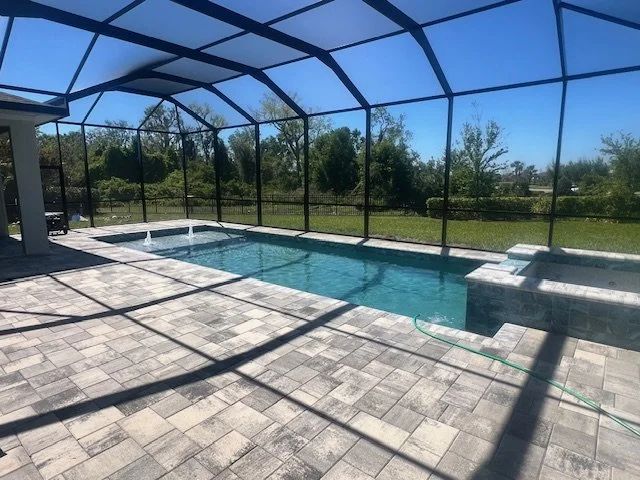A screened rectangular pool with a raised spa and two water bowls on a paver patio.