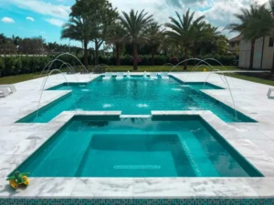 A multilevel geometric pool with a raised sun shelf, water arcs, and in-pool loungers surrounded by marble decking and palm trees.