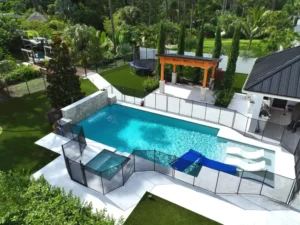 Aerial view of an L-shaped pool with raised spa, in-pool loungers and a stone waterfall wall behind a Florida home on a canal.