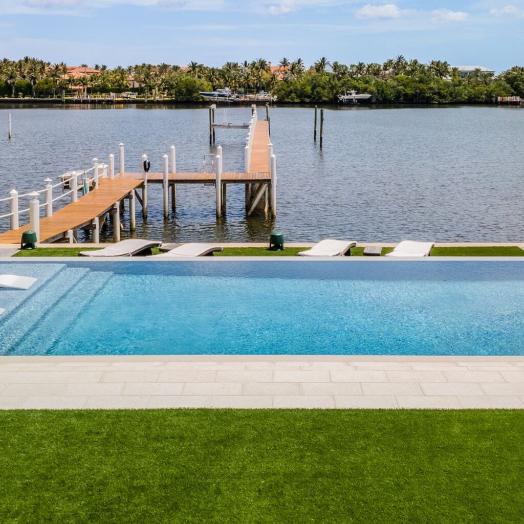 An infinity-edge pool overlooks a calm waterway with a private dock and loungers.