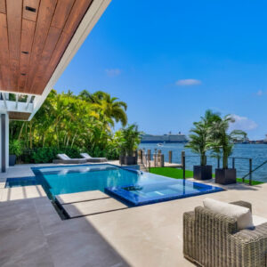 Modern infinity-edge pool with a glass-tiled raised spa overlooking a waterway with a cruise ship passing.
