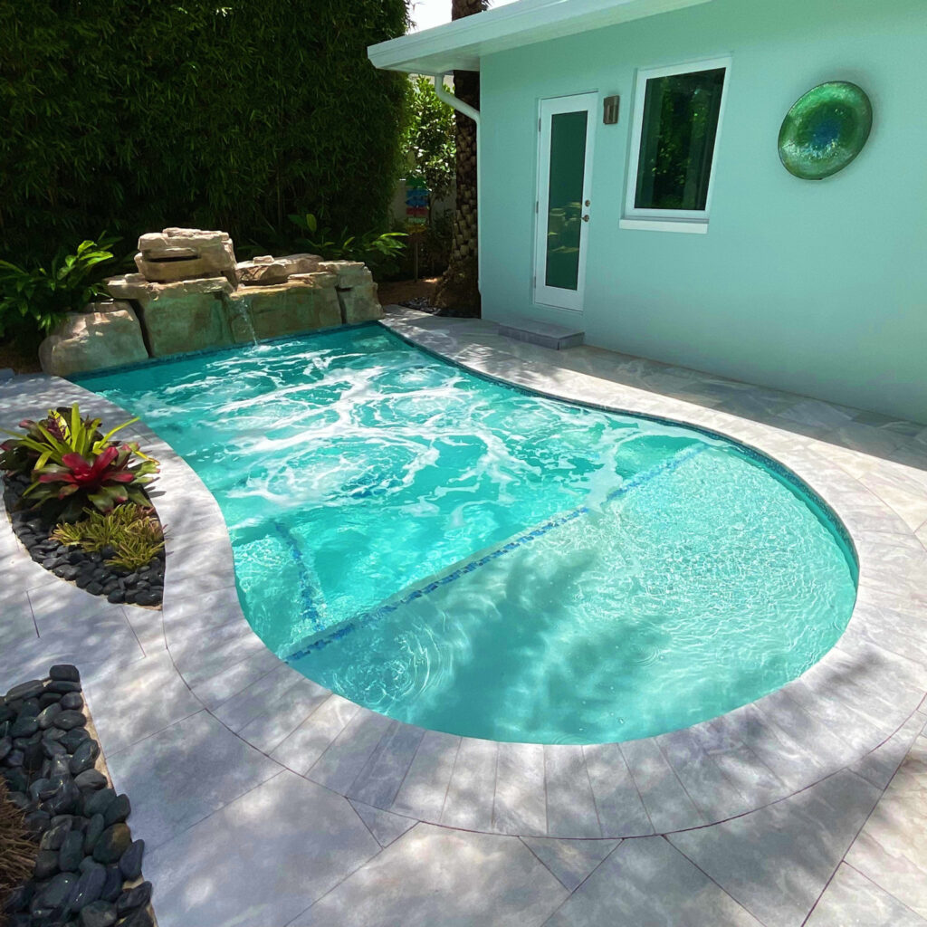 A small freeform pool with a rock waterfall beside a mint-green house patio.