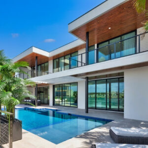 A sleek modern two-story home with a rectangular pool along a stone patio beside the water.