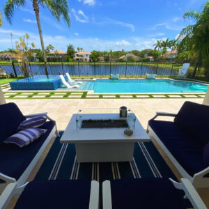 A lakefront backyard pool with a raised tiled spa, in-pool loungers, and a fire pit lounge area in the foreground.