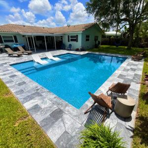 A small rectangular backyard pool with an attached spa, in-pool loungers, and a gray stone tile deck under open sky.