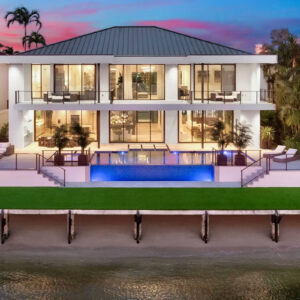 An elevated infinity-edge pool glowing blue at dusk behind a modern waterfront home.
