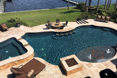 Freeform backyard pool with raised spa, fire bowls, and in-pool loungers overlooking a canal.