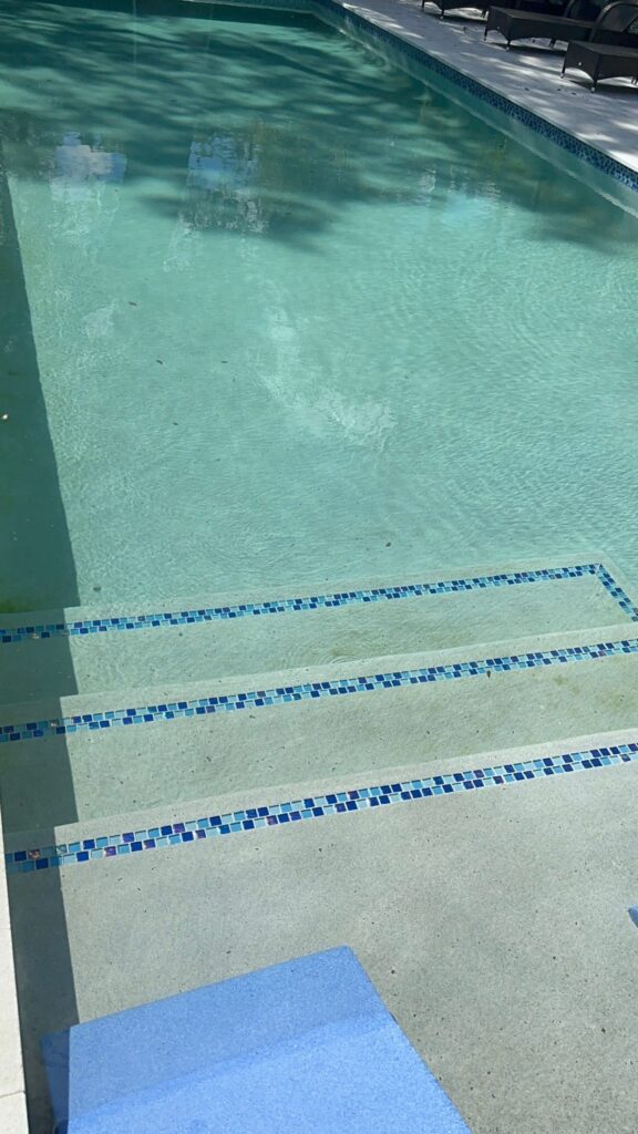 Pool steps trimmed with blue mosaic tile leading into a shaded swimming pool.