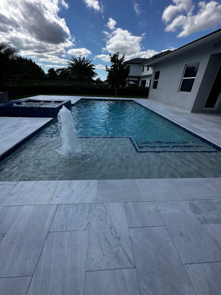A rectangular pool with a bubbler fountain and raised tiled spa beside a modern house.