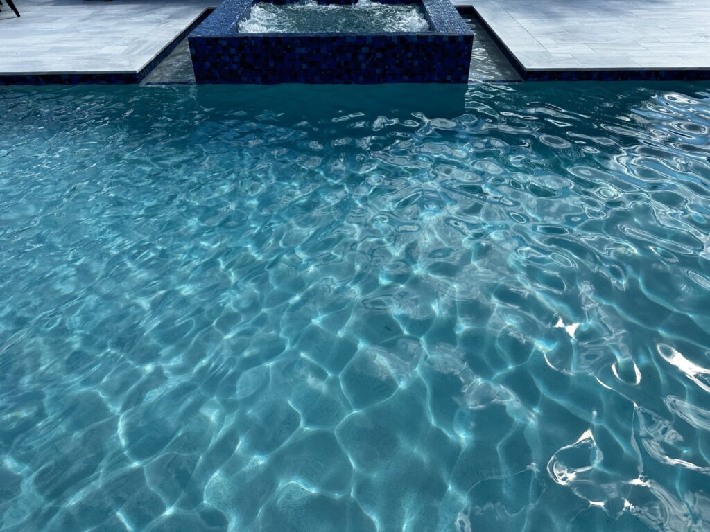 Close-up of a dark mosaic-tiled raised spa with a strip of pool water in the foreground.