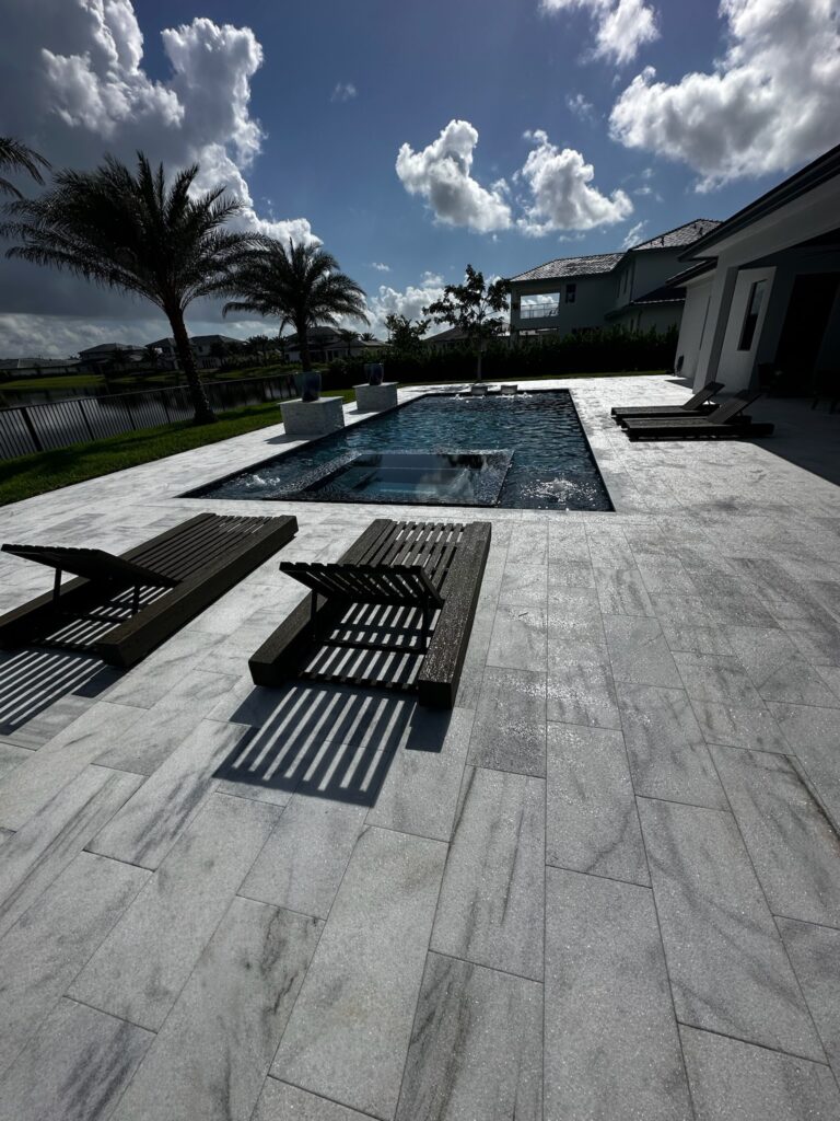 A rectangular pool with an integrated raised-edge spa and water bowls on a stone-paved patio overlooking a canal.