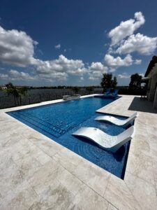 A rectangular lakeside pool with two built-in loungers and a raised spa on a travertine patio.