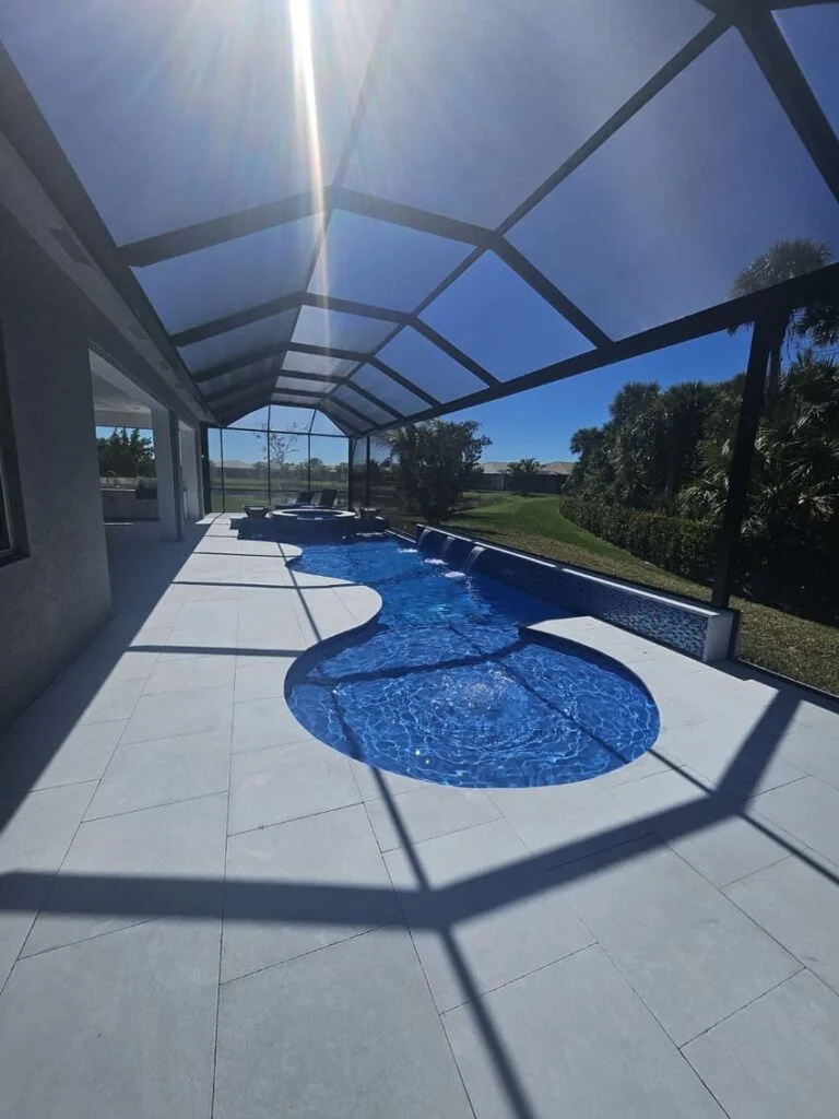 Freeform pool with raised spa and spillover under a screened lanai overlooking a golf course lawn.