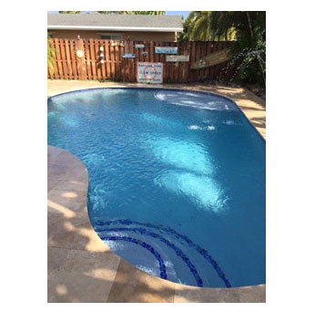 A freeform swimming pool with travertine decking and a wood privacy fence in a backyard.