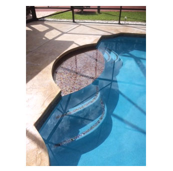 A close view of a pool corner with steps and a decorative mosaic medallion on stamped concrete decking.