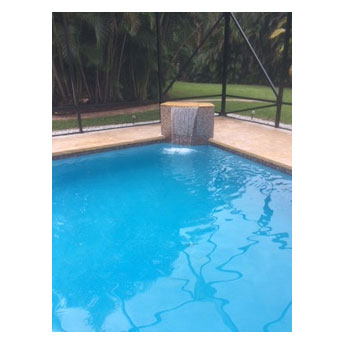 A small rectangular pool with a raised stone water feature under a screened enclosure.