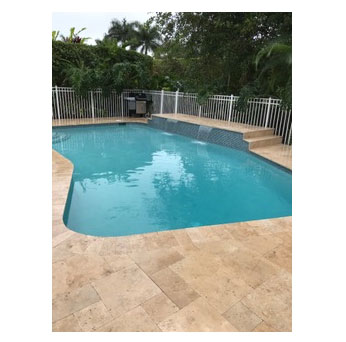 A freeform backyard pool with a raised spa and travertine paver deck, surrounded by a white safety fence and tropical landscaping.